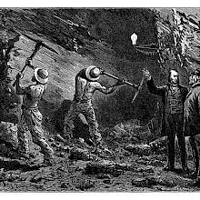 Two miners swing their pickaxes as a man in a suit points to the glow lamp illuminating the scene