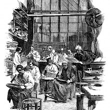 View of a workshop where workers sitting on stools use hammers are shaping flatware