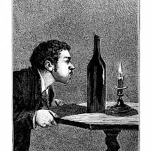 A man leans over a table with his cheeks puffed out to blow out a candle placed behind a bottle