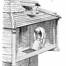 A man is clearing the way for a basket of stones to be delivered through a trap door in the floor of a wooden hoarding