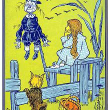 A young girl is sitting on a stile by a cornfield and looks at a scarecrow on a stake