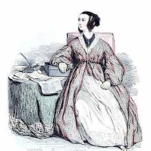 A woman in a dressing-gown is sitting iat a table covered with papers