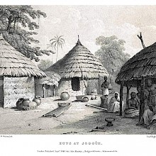 View of a group of huts in an African village, with local people sitting in the shade