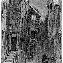 A man walks in the snow carrying a lantern along a narrow street