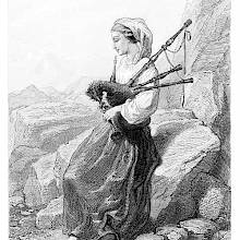 A barefoot woman in country dress is sitting on a rock playing the bagpipe