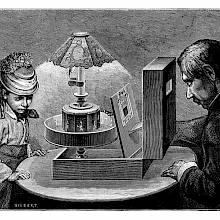 A girl and a man are seen at a table on which a praxinoscope theater has been placed