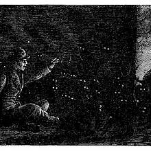 A man sitting in a dark room gestures toward a cat leaning on a cooking pot