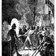 A puddler stands in front of a furnace, maneuvering the hook as a helper stays behind him