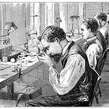 Workshop of a watch factory with men at work sitting on the chairs lining the workbench