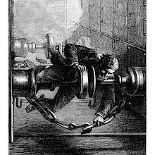 A man is precariously balanced on the buffer of a moving locomotive as he attempts to uncouple it from the luggage car