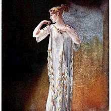 A woman stands against a strongly contrasted background wearing a dress in the Greek style
