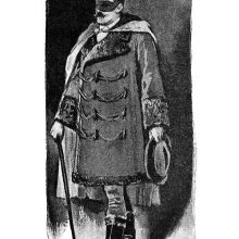 A masked man with a cane stands wearing a frogged coat and a cape