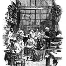 View of a workshop where workers sitting on stools use hammers to craft flatware