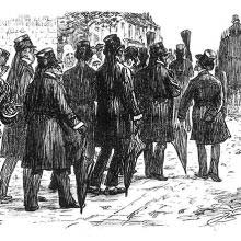 Men wearing a black hatbands are seen from behind following a hearse