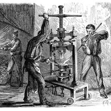 View of a workshop where two men are busy around a mobile press for molding goblets