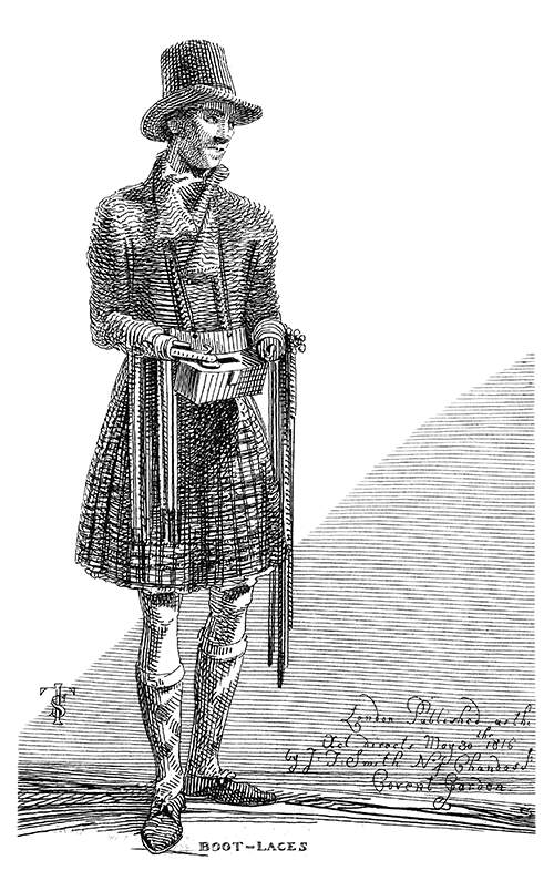 A man in a kilt and a coachman hat and missing both his hands sells boot laces in the street
