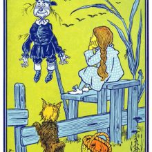 A young girl is sitting on a stile by a cornfield and looks at a scarecrow on a stake