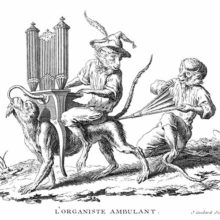 A monkey walks on all fours with an organ and another monkey on its back, a third one following