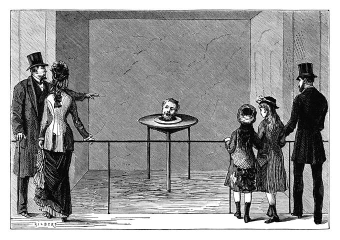 An small audience looks at a table on which the severed head of a man is staring back and talking