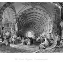 View of a covered street lined with stalls on both sides showing a carpet seller in the foreground