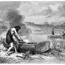 A prehistoric man wearing animal skin makes a boat from a piece of tree trunk